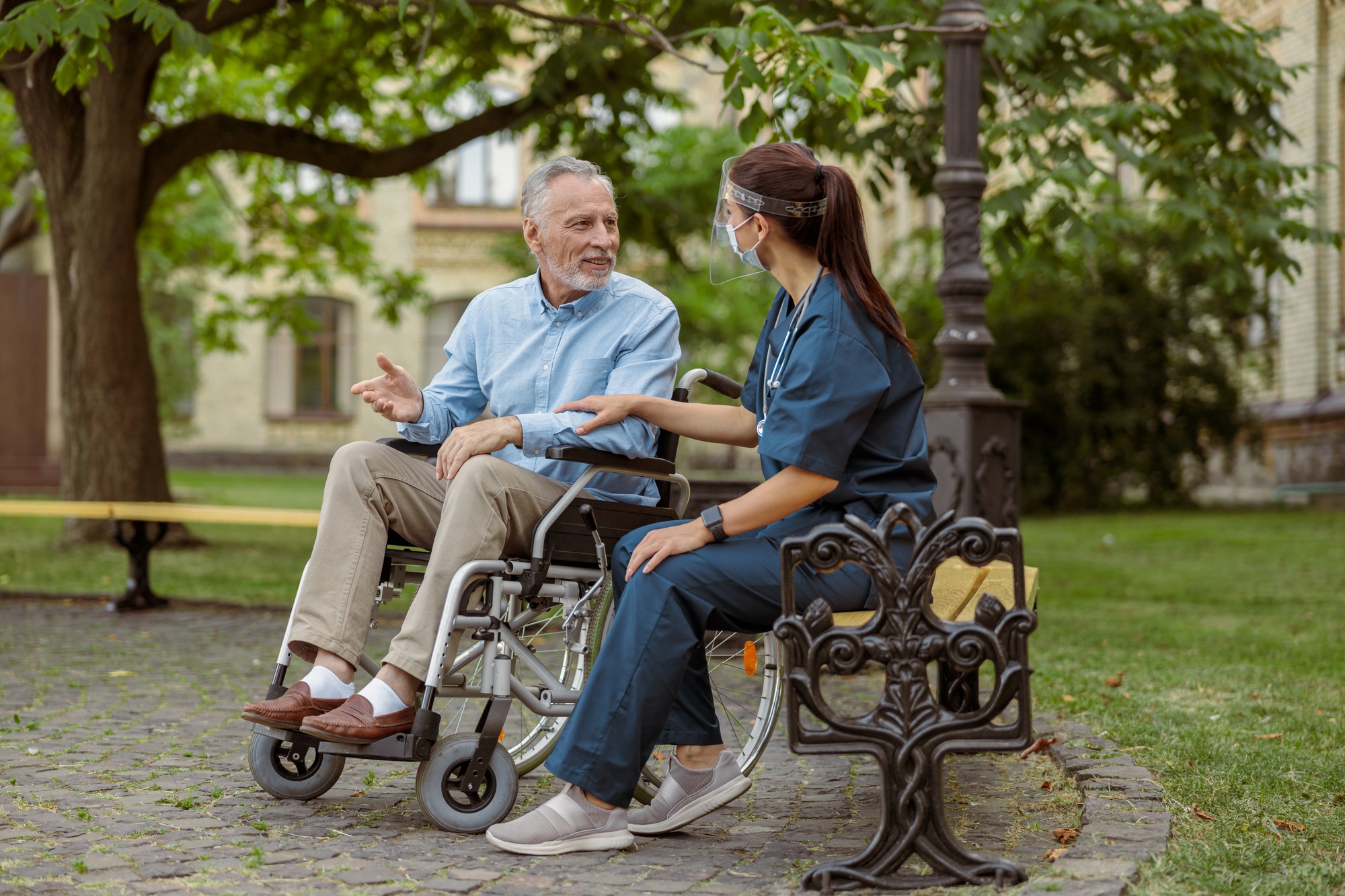 Full length shot of cheerful mature man, recovering patient in wheelchair talking to caring nurse